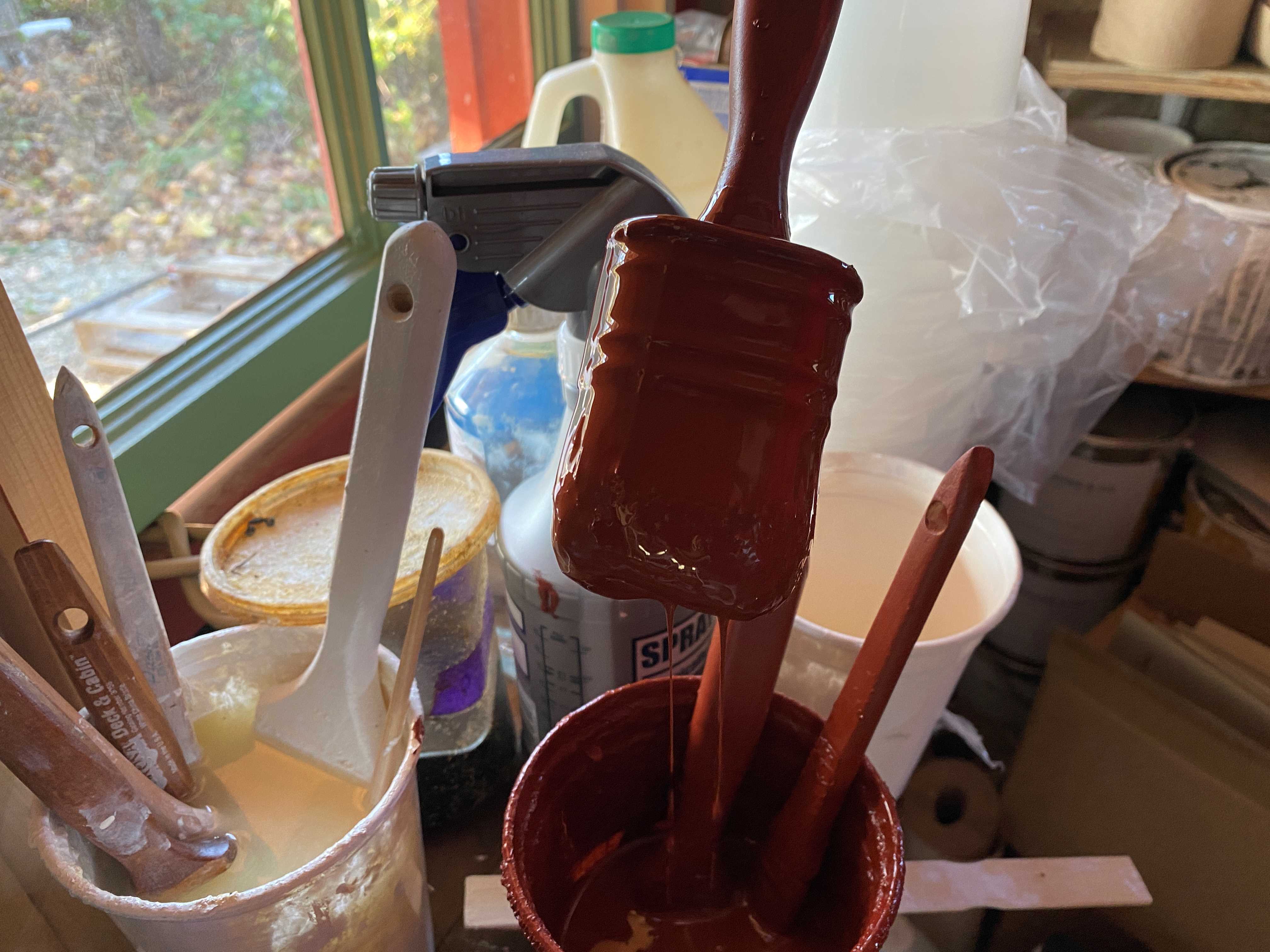 photo of a paint brushes sitting in small pots of paint on a shelf in front of a window